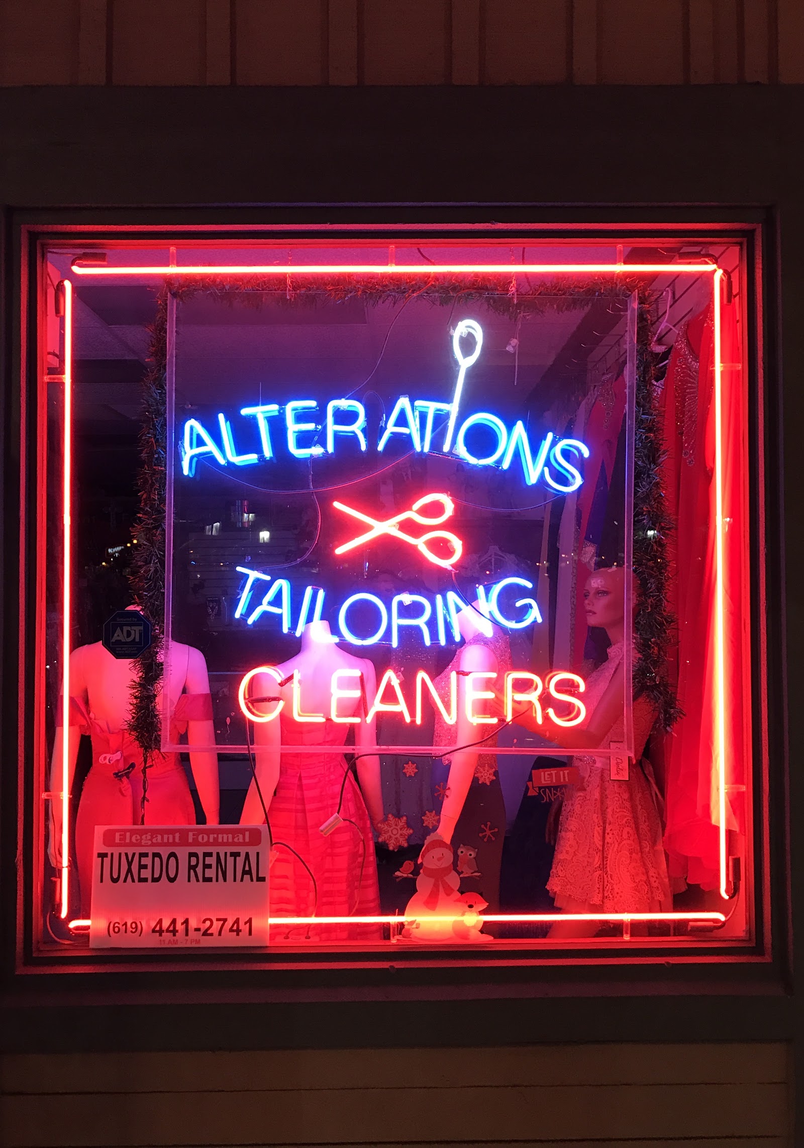 Neon window sign: Alterations, Tailoring and Cleaners with formal gowns on display